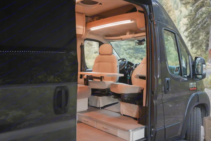 Inside a modern rv rental camper van: swiveling light-colored seats, a movable dining table, and LED strip lighting.. Thor Rize 2022