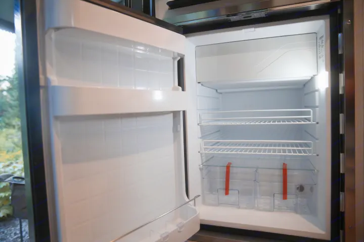 Empty, clean RV rental refrigerator interior, ready for your travel essentials, featuring wire shelves and crisper bins.. Thor Rize 2022