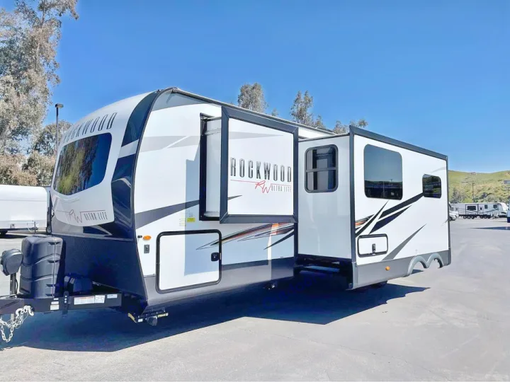 A white & black Rockwood travel trailer, ideal for RV rental, with its slide-out extended. Parked outdoors on a sunny day.. Forest River Rockwood Ultra Lite 2022