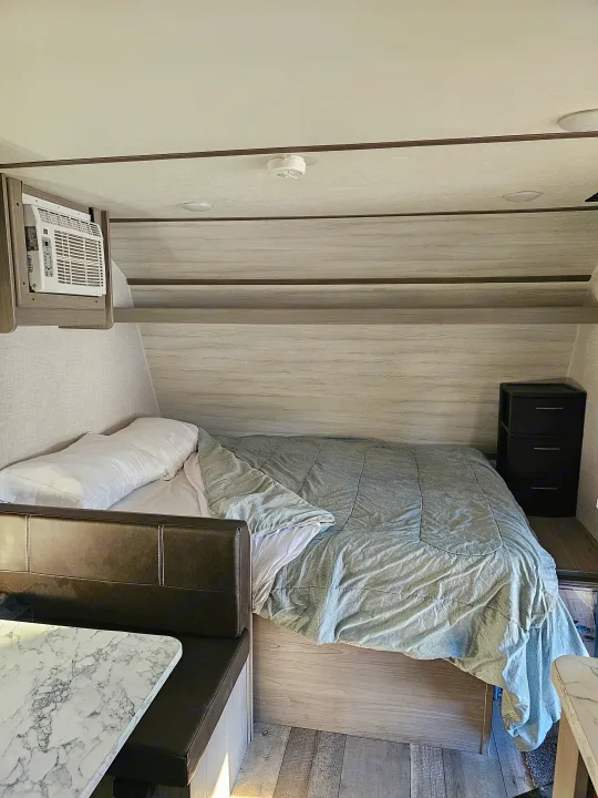 Cozy RV rental bedroom featuring a comfy bed, compact dinette, AC, and bedside storage for your adventures.. Dutchmen Coleman 17B 2023