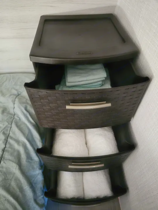 Dark brown, 3-drawer storage unit in an RV rental. Top drawer has blue cloths, others hold white towels.. Dutchmen Coleman 17B 2023