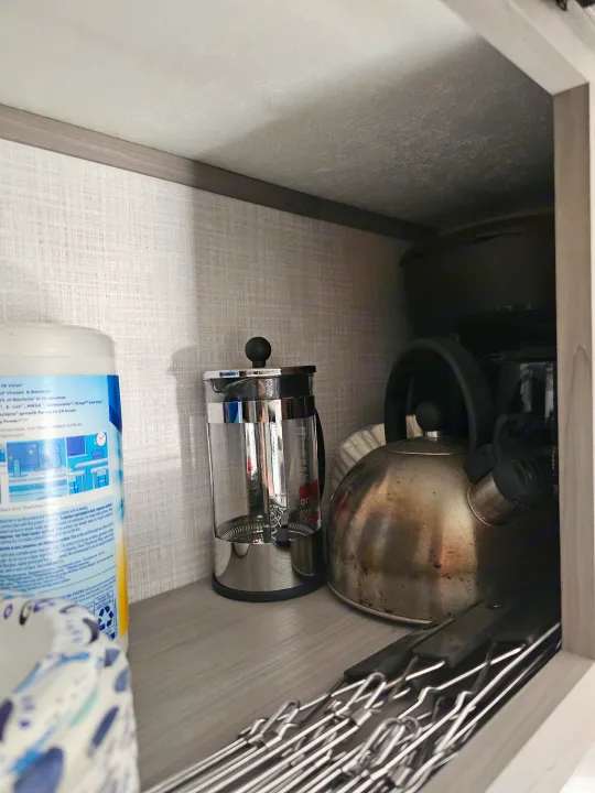 Kitchen essentials in an RV rental cabinet: a French press, kettle, skewers, and cleaning wipes for convenient living.. Dutchmen Coleman 17B 2023