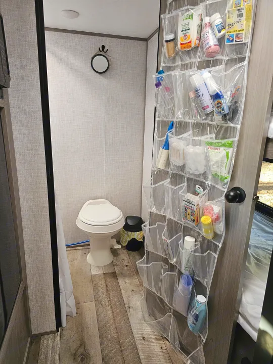An RV rental's small bathroom showcasing clever over-the-door storage for toiletries, first aid, and camping essentials.. Dutchmen Coleman 17B 2023