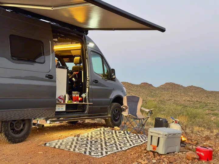 Enjoy the desert sunset with this cozy rv rental setup. Camper van with open door, awning, and outdoor living area.. Winnebago Revel 2024