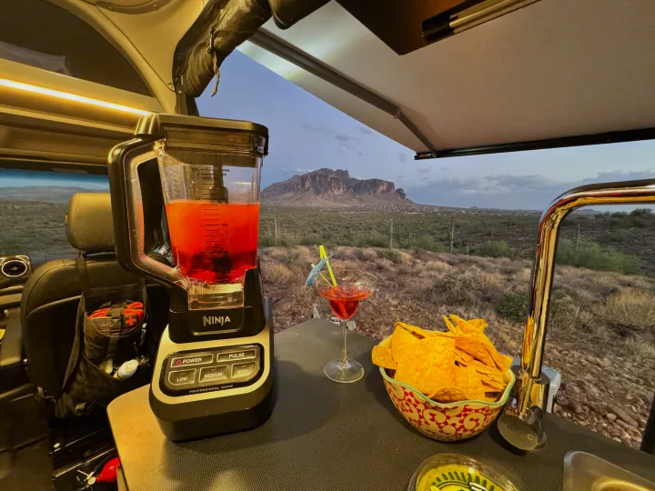 RV rental adventure: Enjoying cocktails & chips with a blender setup and stunning desert mountain views from inside a camper van.. Winnebago Revel 2024