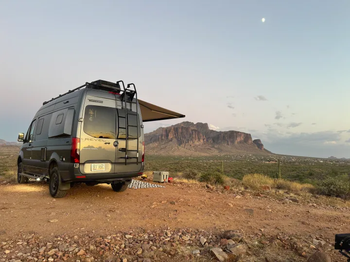 RV rental campervan parked in desert with mountains, cooler, campfire, and moonlit sky. Ideal for adventure and boondocking.. Winnebago Revel 2024
