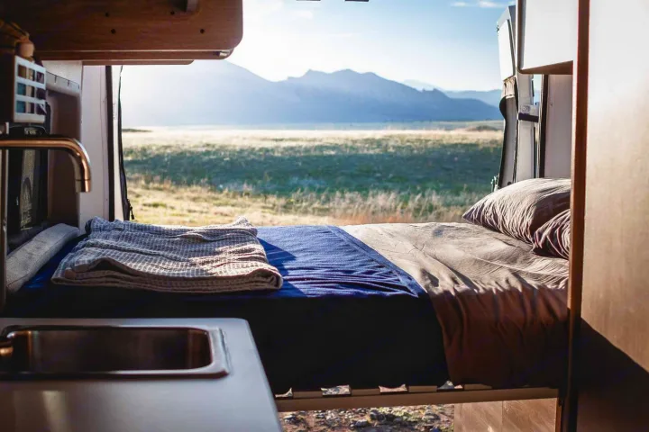 Experience nature with an RV rental! Cozy bed & sink inside a camper van, offering stunning mountain views & open fields.. Winnebago Solis 2023