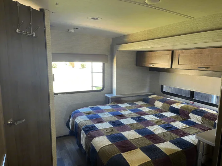 Step into comfort: a cozy RV rental bedroom featuring a patchwork quilt, ample overhead storage, and natural light from a large window.. Winnebago Sunstar 2021