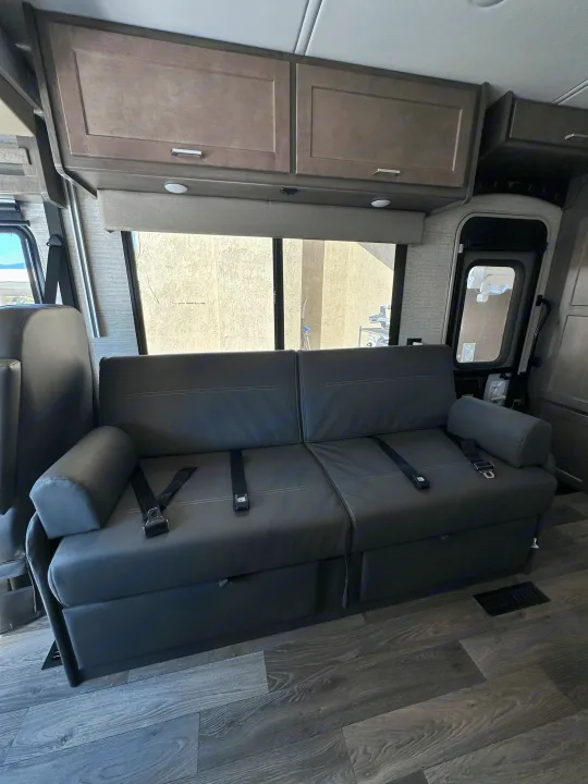 RV rental interior showcasing comfy sofa seating with seatbelts, overhead cabinets, and wood-look flooring. Ready for your adventure.. Winnebago Sunstar 2021