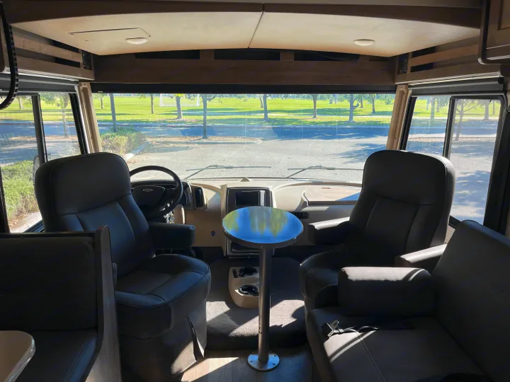 Spacious RV rental interior showing the cockpit, comfortable captain's chairs, and a small table with a park view.. Winnebago Sunstar 2021