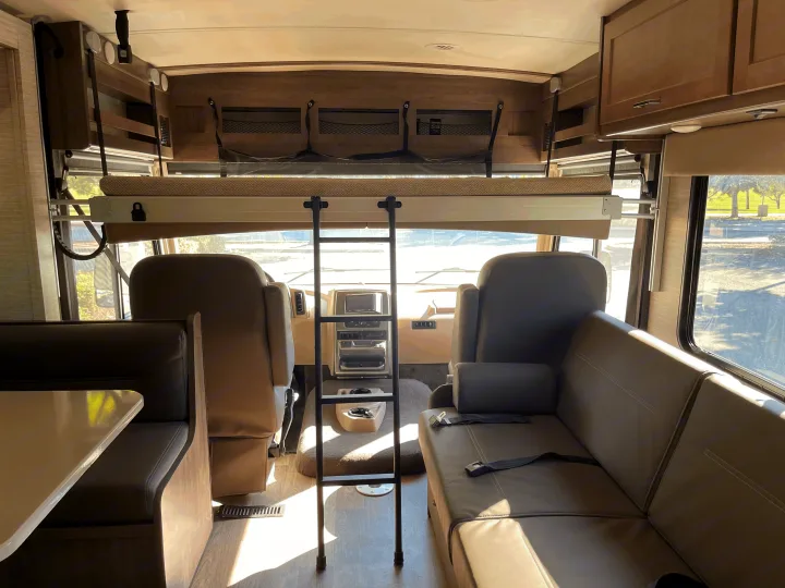RV rental interior featuring a drop-down bunk bed with ladder, cab, dinette, and sofa seating for a spacious travel experience.. Winnebago Sunstar 2021