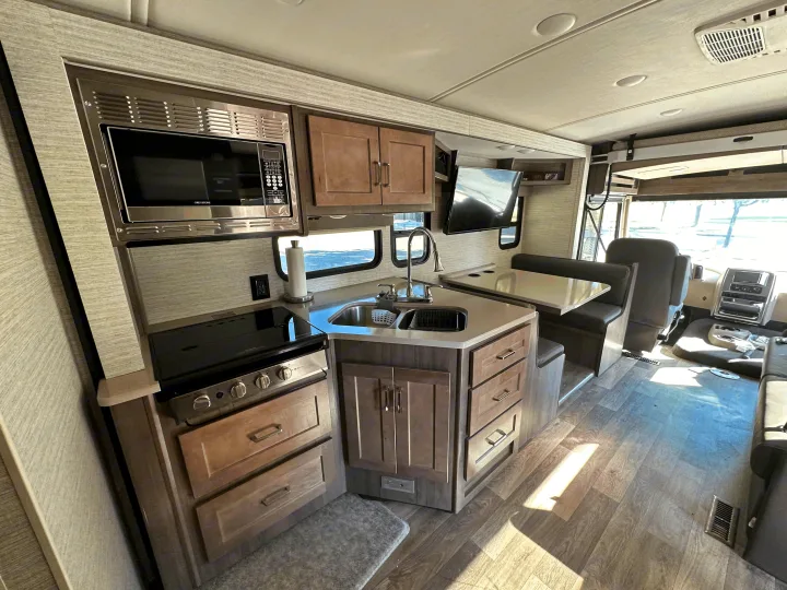 An RV rental's modern kitchen area, featuring a microwave, stove, sink, and dining booth. Bright and inviting.. Winnebago Sunstar 2021