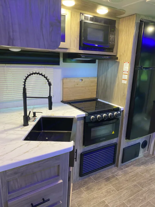 Spacious RV rental kitchen showcasing a modern black sink, microwave, stove/oven, and ample counter space for travel.. Forest River Cherokee Alpha Wolf 2022