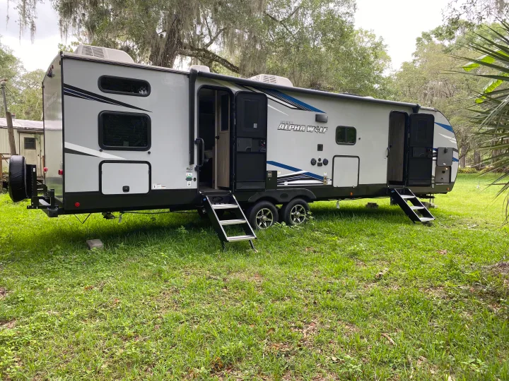 Modern travel trailer RV rental parked on grass, steps extended. Perfect for your next camping adventure.. Forest River Cherokee Alpha Wolf 2022