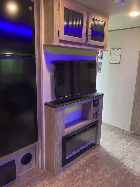 Modern RV rental interior with TV, electric fireplace entertainment unit, refrigerator, and light wood cabinets.. Forest River Cherokee Alpha Wolf 2022