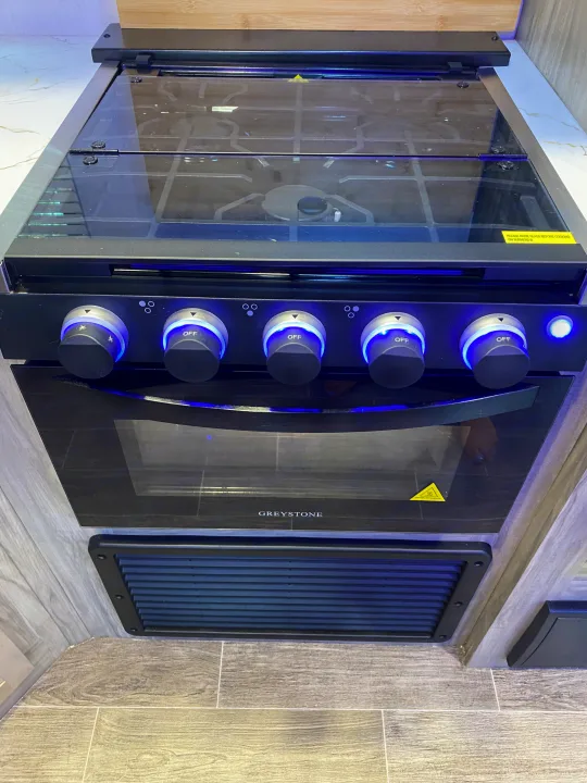 Modern Greystone RV stove/oven with illuminated controls, perfect for an rv rental. Note the glass cover & safety warning.. Forest River Cherokee Alpha Wolf 2022