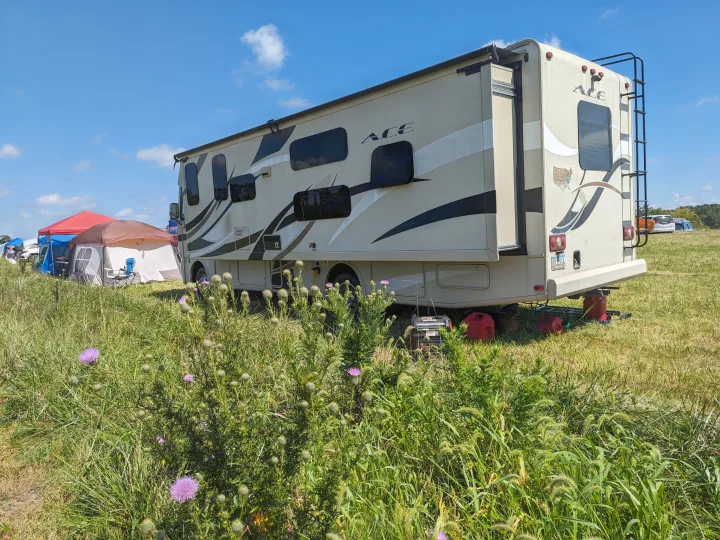 RV rental parked in a grassy field with extended slide-out, generator, and gas cans. Tents nearby for camping.. Thor ACE 30.2 2015