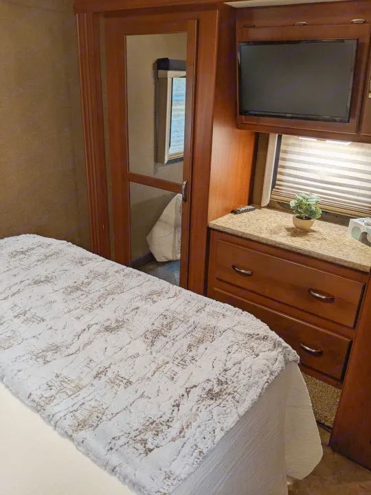 Cozy RV rental interior, featuring a bed with textured bedding, a mirrored closet, TV, and counter with storage drawers.. Thor ACE 30.2 2015
