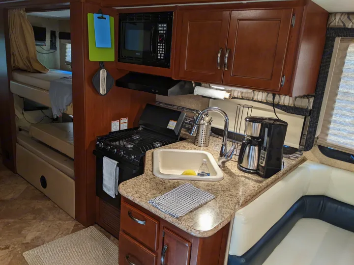 An RV rental's efficient kitchen, complete with stove, microwave, sink, and coffee maker, next to cozy bunk beds.. Thor ACE 30.2 2015