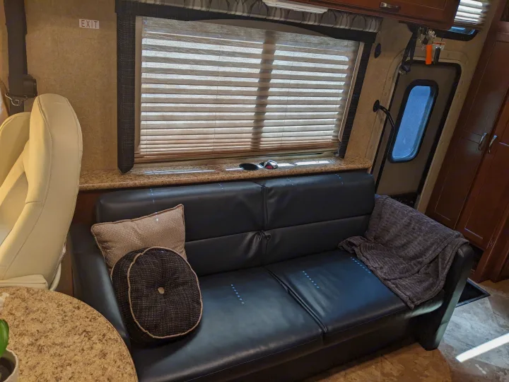 Inside this RV rental: black leather sofa, window blinds, and exit door are visible, offering comfort for your journey.. Thor ACE 30.2 2015