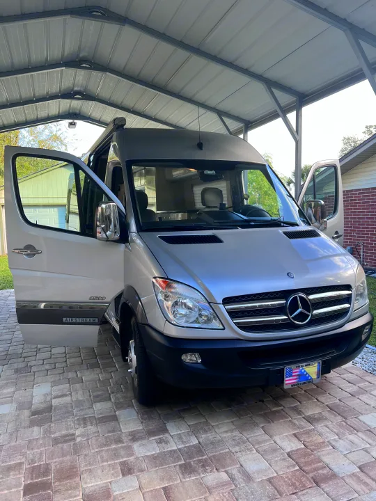 Silver Airstream Mercedes Sprinter RV rental camper van parked under a carport with doors open on pavers.. Airstream Interstate 2012