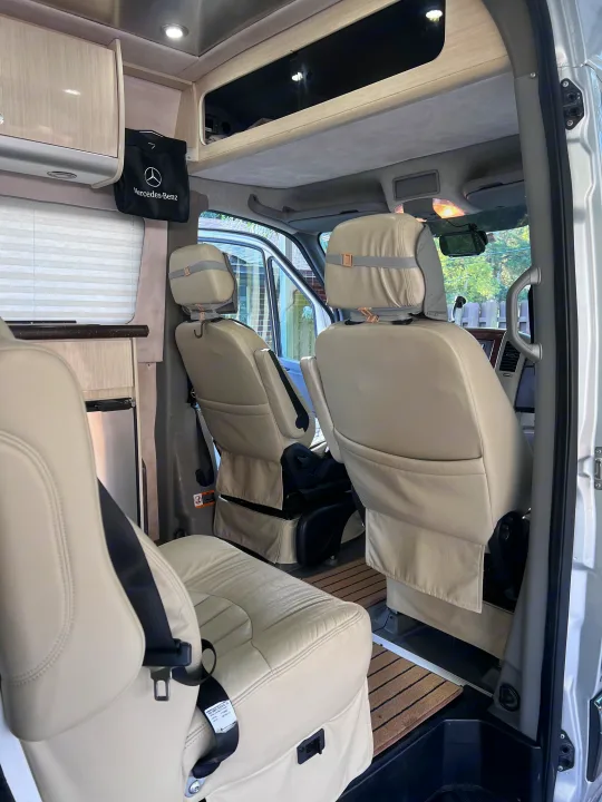 View inside an RV rental showing cream leather seats, overhead storage, and a small fridge. This comfortable cabin is ready for travel.. Airstream Interstate 2012