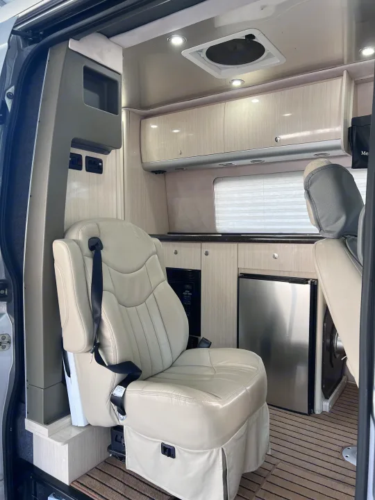 Clean and modern RV rental interior featuring a cream leather captain's chair, compact kitchen, fridge, and overhead cabinets.. Airstream Interstate 2012