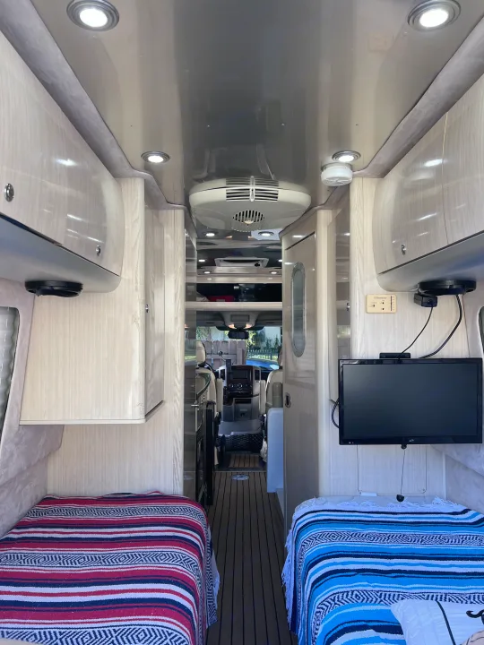 RV rental interior: A bright, modern compact living space with twin beds, overhead cabinets, and a view to the cockpit.. Airstream Interstate 2012