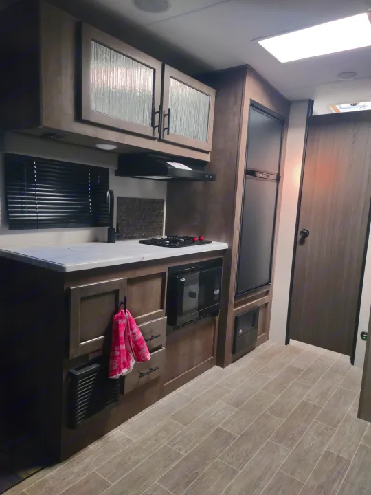 Explore this modern rv rental's well-equipped kitchen: sleek cabinets, sink, stove, microwave, and fridge, all with plank flooring.. Sonic Lite 2021