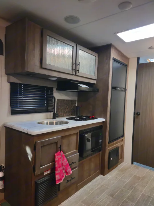 RV rental kitchen interior: modern cabinets, sink, two-burner stove, microwave, fridge, & window blinds.. Sonic Lite 2021