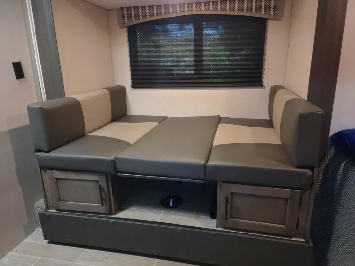 RV rental interior: cozy dinette seating converted to a bed with stylish gray cushions & wood cabinets.. Sonic Lite 2021