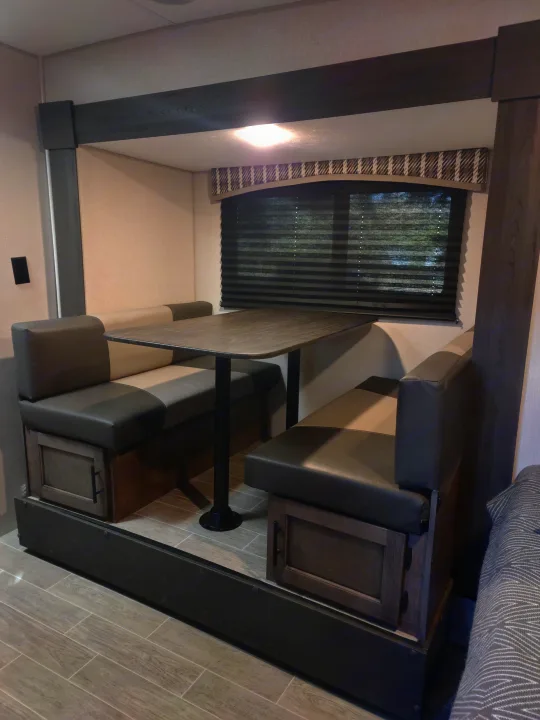 Spacious RV rental dinette area featuring upholstered bench seats with storage, a central table, and window blinds.. Sonic Lite 2021