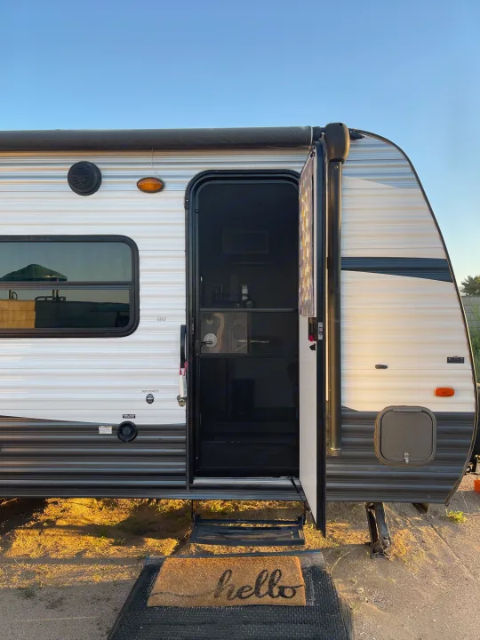 Your cozy rv rental awaits! Side view of a travel trailer with open screen door & "hello" doormat.. Keystone RV Summerland Mini 2017