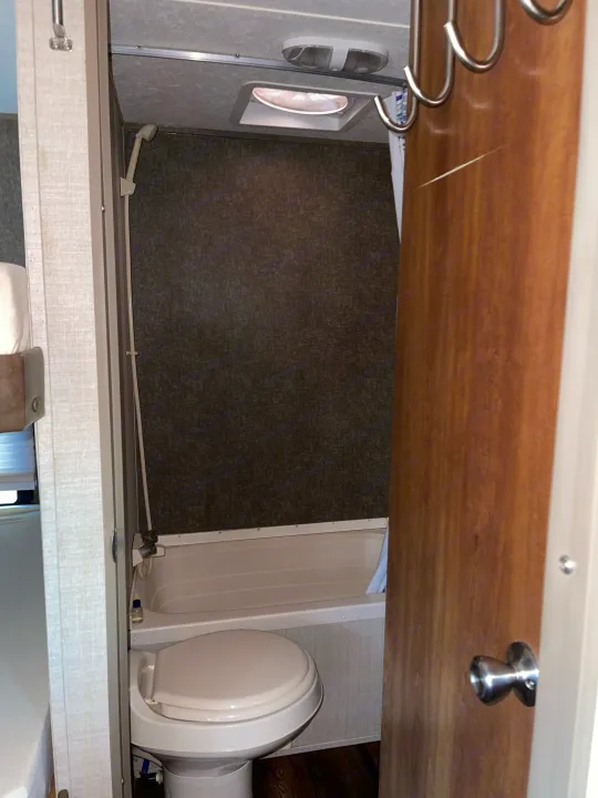 Inside an RV rental: a compact wet bath with toilet, shower, ceiling fan, and door hooks.. Keystone RV Summerland Mini 2017