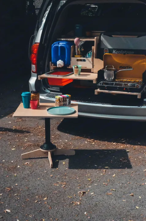 RV rental van life: compact kitchen setup in a silver van, featuring a stove, sink, water, and an outdoor dining table.. Chrysler Grand Caravan 2022
