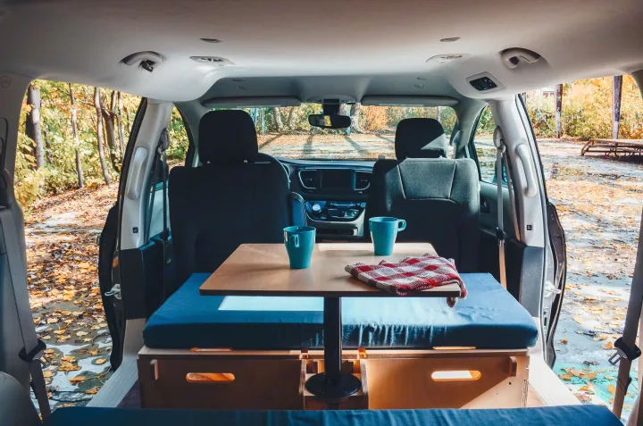 Cozy rv rental campervan interior: table with mugs, seating, and vibrant autumn forest views outside.. Chrysler Grand Caravan 2022