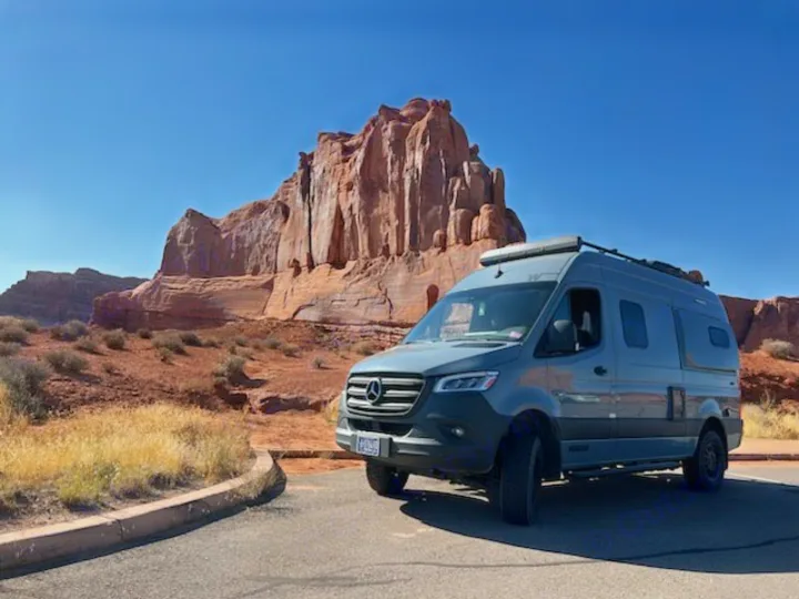 Gray Mercedes-Benz RV rental van parked before vast red rock formations. Perfect for desert adventure travel.. Winnebago Revel 2022