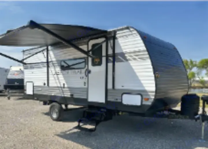 RV rental: A white and gray travel trailer with an extended awning, parked on gravel. Ideal camper for adventure.. Aspen Trail LE 2024