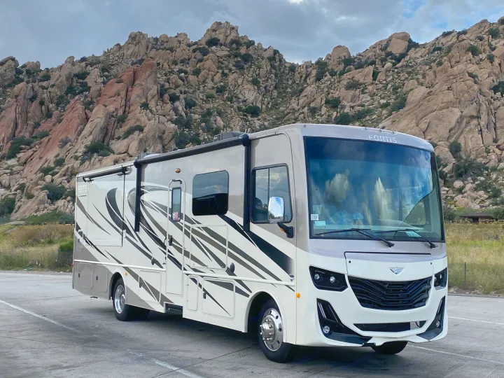 Spacious RV rental parked against a backdrop of rugged mountains under a cloudy sky. Ideal for road trips and adventure.. Fleetwood Fortis 2021