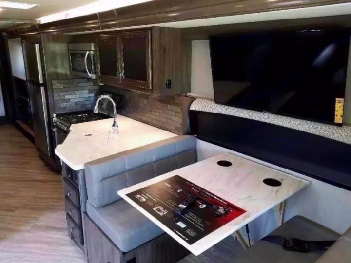 Modern RV rental interior featuring a full kitchen, dining booth, & wall-mounted TV.. Fleetwood Fortis 2021