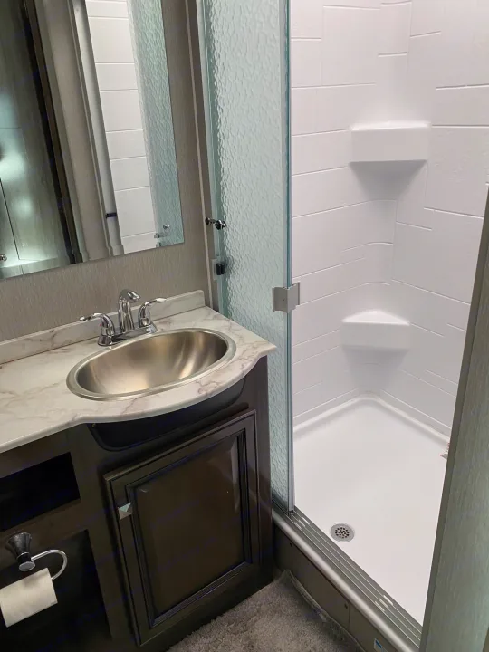 Clean RV rental bathroom featuring a vanity with a sink, mirror, and modern glass-enclosed shower with built-in shelf.. Fleetwood Fortis 2021