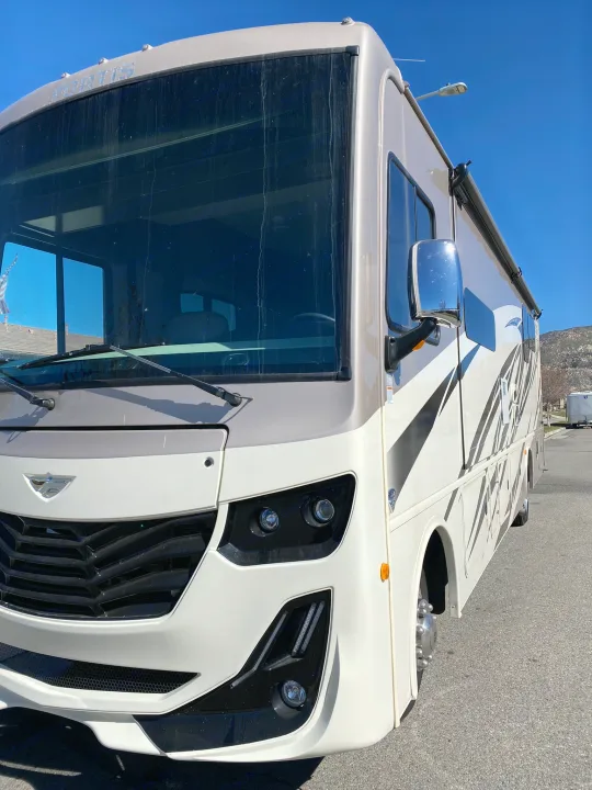 Front view of a cream and beige Fortis RV rental motorhome with dark graphics, parked on asphalt under a clear sky.. Fleetwood Fortis 2021