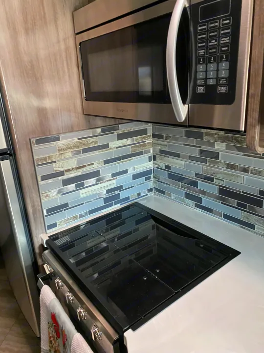 Modern RV rental kitchen featuring an Insignia microwave, sleek cooktop, and stylish backsplash for easy meal prep.. Fleetwood Fortis 2021