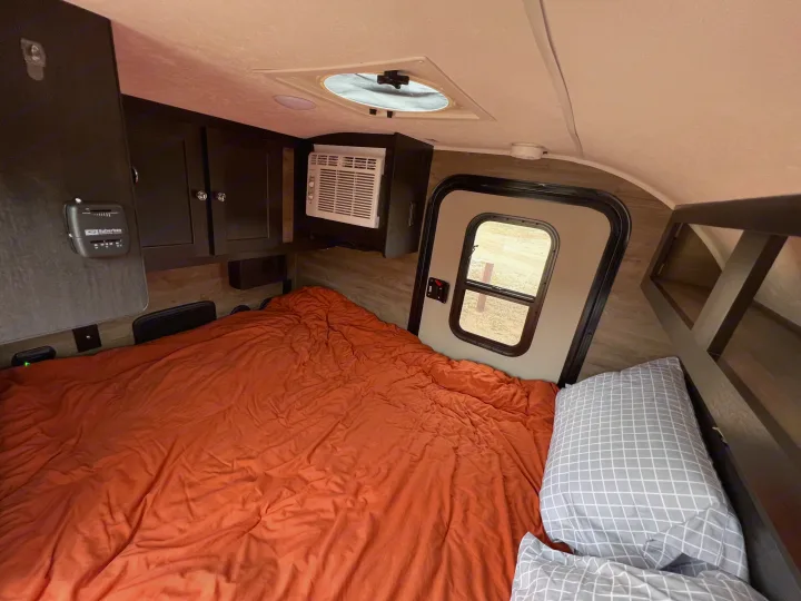 This rv rental shows a cozy bedroom with an orange bed, AC unit, thermostat, and storage, perfect for your next trip.. Braxton Creek Free Solo 2022