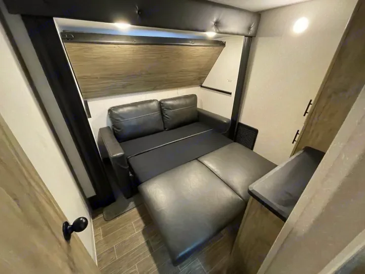 Comfortable RV rental interior featuring a black convertible sofa that extends into a lounge or bed, perfect for travel.. Forest River Cherokee Arctic Wolf 2022