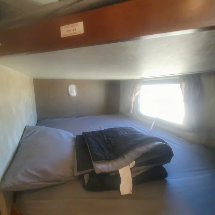 Cozy RV rental bunk bed setup with a pillow, comforter, and a 'DO NOT EXCEED 250 LBS' sign above.. Winnebago Ultralite 2014