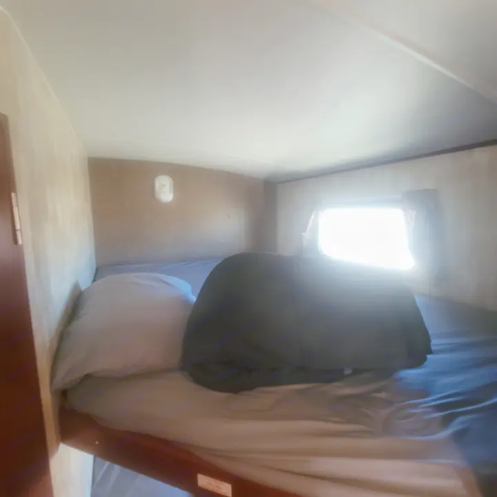 Inside an RV rental: a compact bunk bed area with a pillow, rolled dark blanket, and bright window. Ready for your adventure.. Winnebago Ultralite 2014