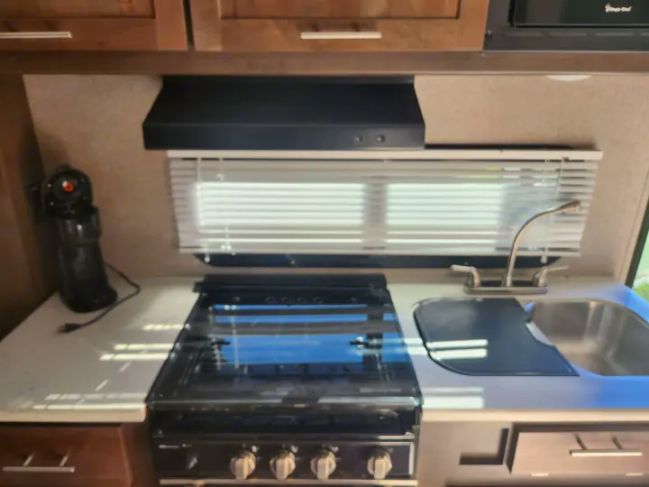 RV rental kitchen: wood cabinets, range hood, window, coffee maker, stovetop, and sink.. Forest River Rockwood Mini Lite 2019