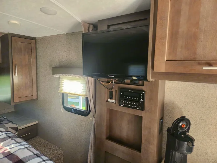 RV rental bedroom with plaid bedding, bedside table, mounted TV, stereo system, and coffee maker. A well-equipped interior.. Forest River Rockwood Mini Lite 2019