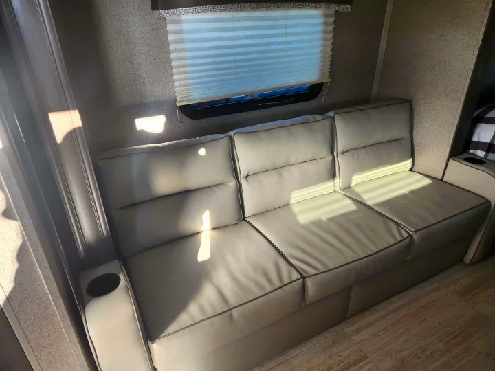 Comfortable grey sofa with cup holders in an RV rental interior, illuminated by sunlight through the window with blinds.. Forest River Rockwood Mini Lite 2019